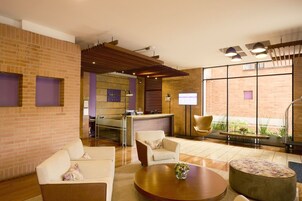 A hotel lobby with a reception desk, seating area, and a view of the outside.