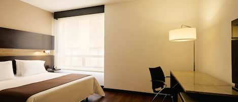 Ein Hotelzimmer mit Bett, Nachttisch, Lampe und Blick ins Freie.