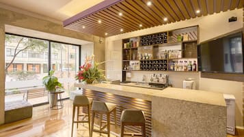 Zona de bar moderna con mostrador, taburetes y una variedad de botellas y vasos.