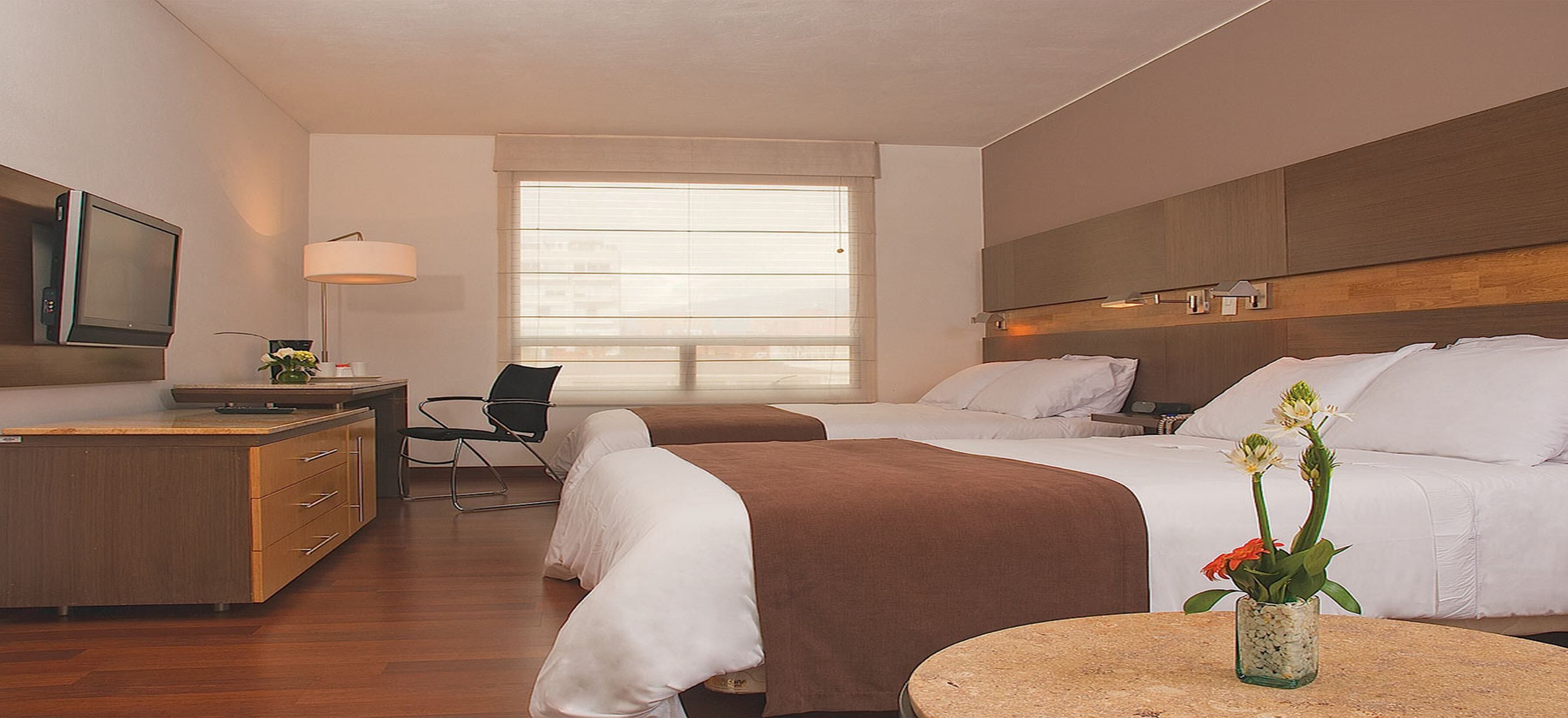 A hotel room with a bed, a desk, a chair, a TV, and a window.