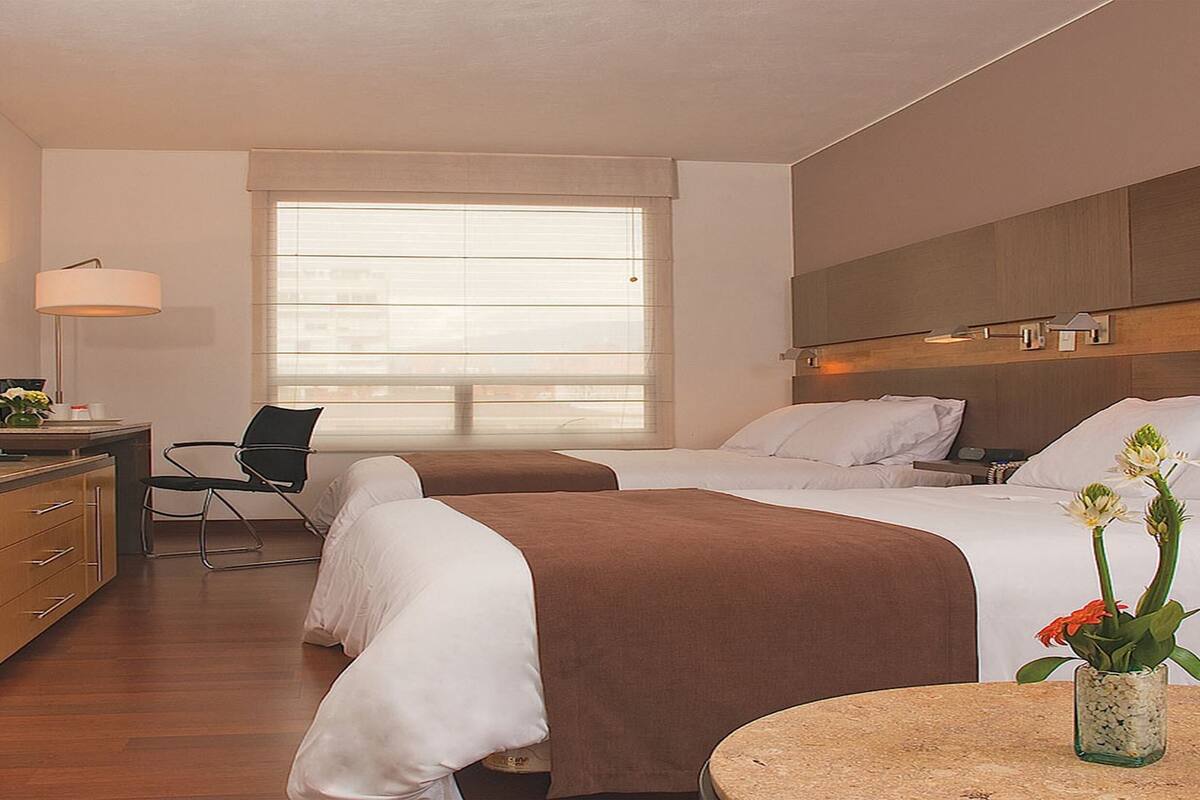 A hotel room with a bed, a desk, a chair, a TV, and a window.