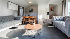 En moderne stue med en grå sofa, et rundt sofabord og et spiseområde med træmøbler.