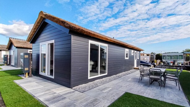 Una casa moderna con esterno scuro, ampie finestre e una veranda con mobili da esterno.