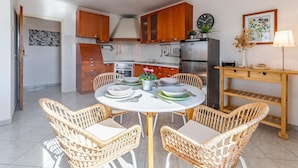 Une cuisine moderne avec des meubles en bois, un réfrigérateur en acier inoxydable et un coin repas comprenant des chaises en osier et une table ronde.
