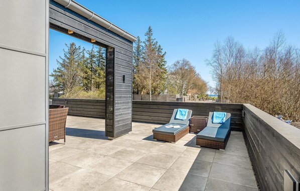An outdoor patio with two lounge chairs and a small table, surrounded by a low wall and trees in the background. - Amazing home in Hadsund with WiFi (Hadsund)