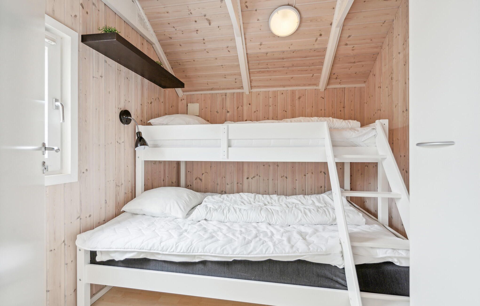 A bunk bed room with a wooden ceiling and walls, a small shelf with plants, and a door on the left.