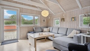 Ein modernes Wohnzimmer mit einem grauen Ecksofa, einem Holztisch und einem großen Fenster mit Blick auf Grünflächen.