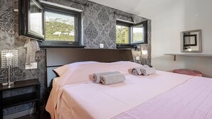 Een slaapkamer met een groot bed, twee nachtkastjes, een spiegel en een raam met uitzicht op groen en bergen.
