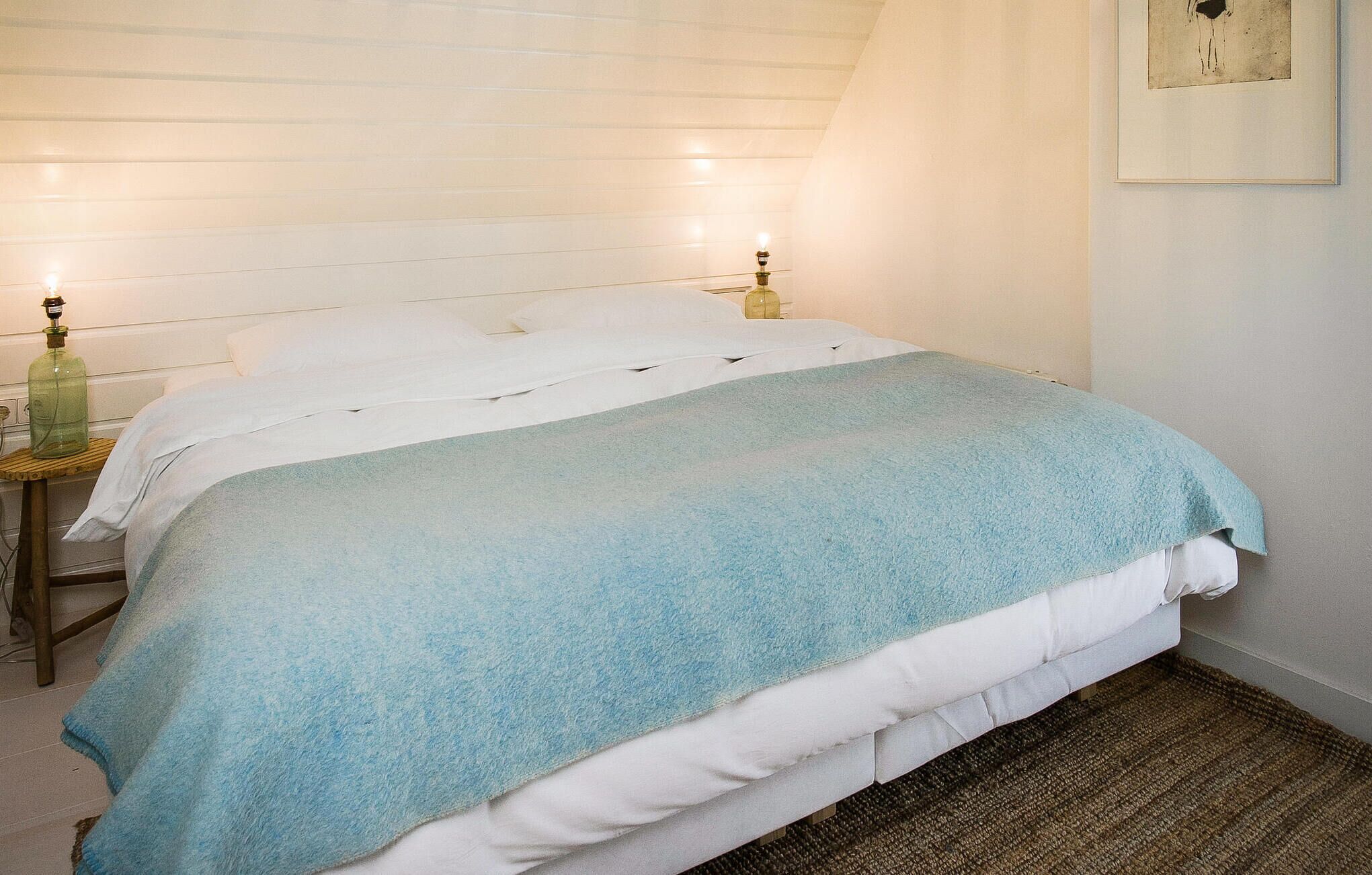 Un dormitorio con una cama, dos lámparas de noche y un cuadro en la pared.