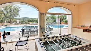 Una habitación con mesa de fútbol de mesa, piscina y mobiliario de exterior.