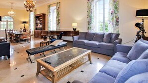 Un salón amplio con un sofá, un sillón y una mesa de centro. Hay un comedor con una mesa y sillas, y una estantería llena de libros.