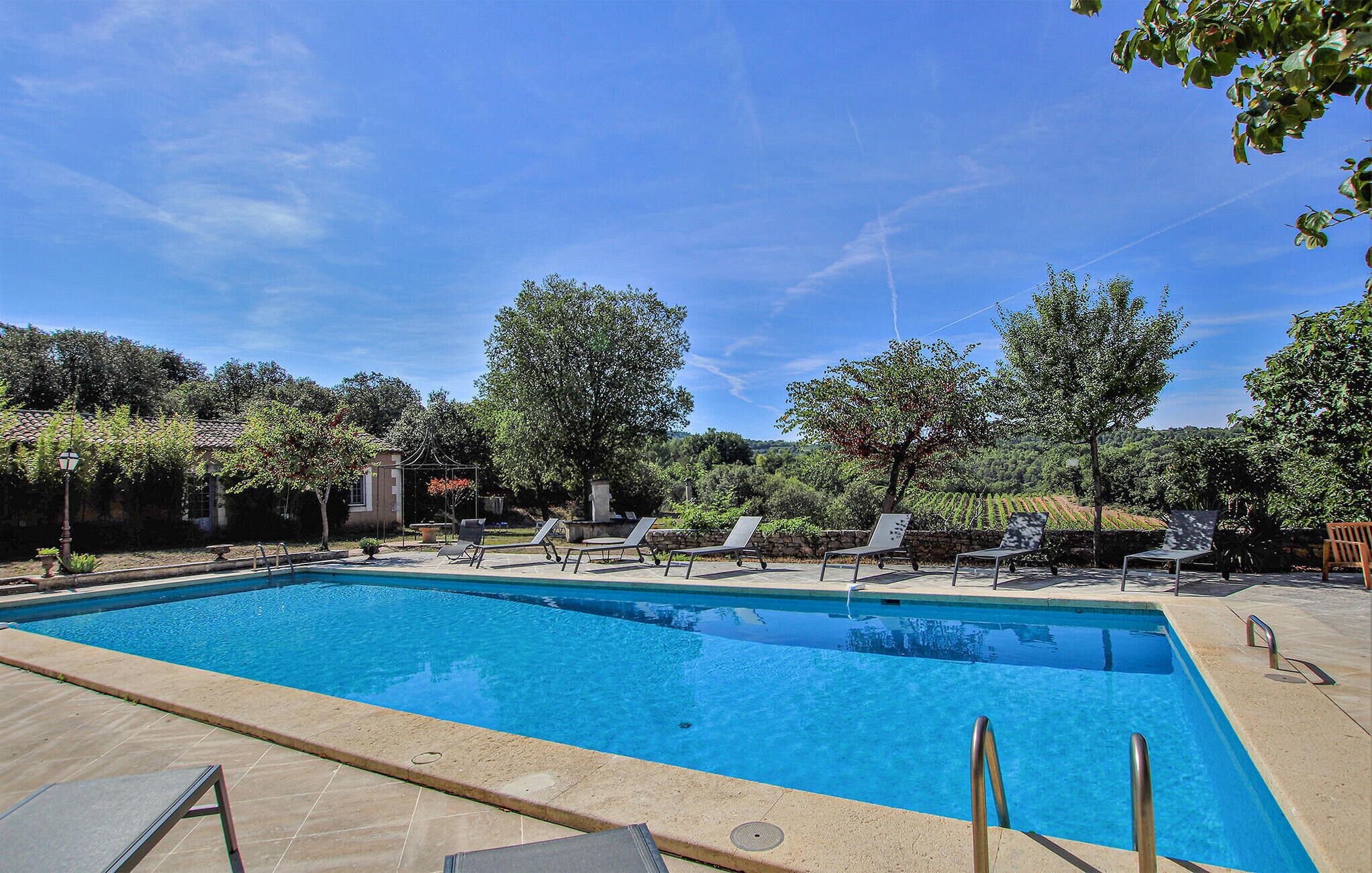 Piscina rectangular con borde de azulejos, rodeada de sillas de descanso y una pérgola.
