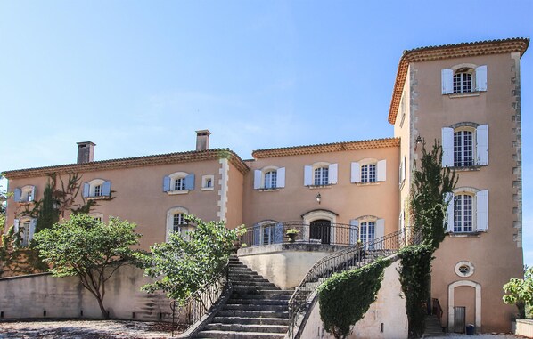 Un edificio histórico con una escalera central, varias ventanas con contraventanas y una balaustrada de piedra.