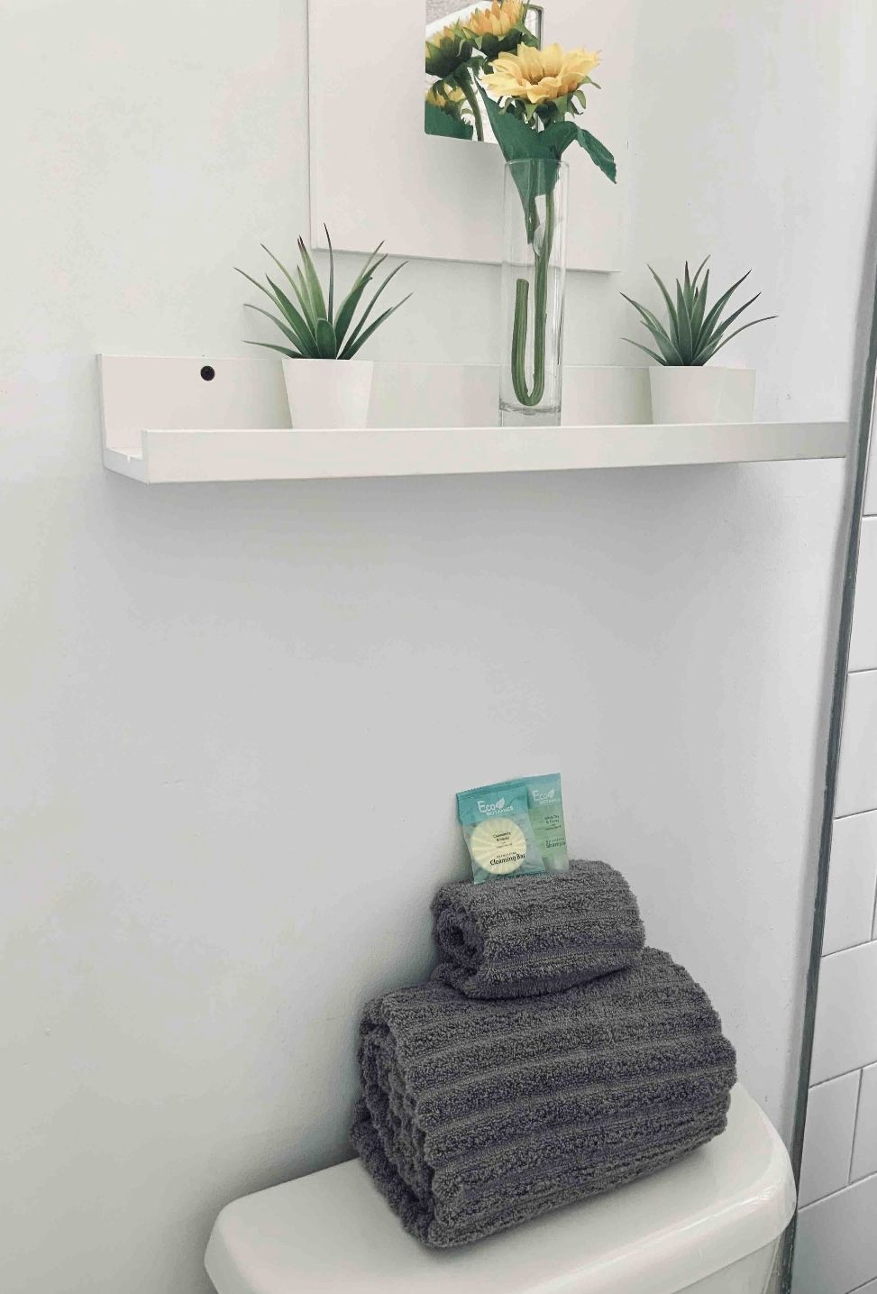 Un baño con inodoro blanco, una toalla y un estante con plantas y un florero.