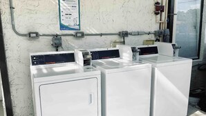 A laundry facility with three white washing machines and a control panel.