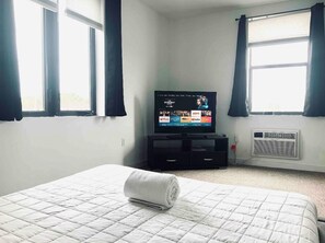 Una habitación de hotel con cama, un televisor mostrando una película y una ventana con cortinas.