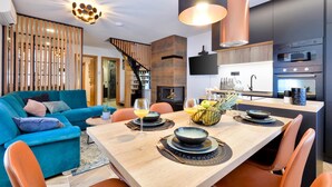 Ein modernes Wohnzimmer mit einem blauen Sofa, einem Esstisch mit Tellern und Gläsern sowie einer Küchenzeile mit Mikrowelle und Backofen.