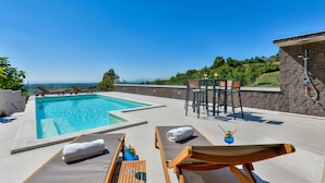 Ein Poolbereich mit Liegestühlen, einem Tisch mit Getränken und Blick auf die Landschaft.