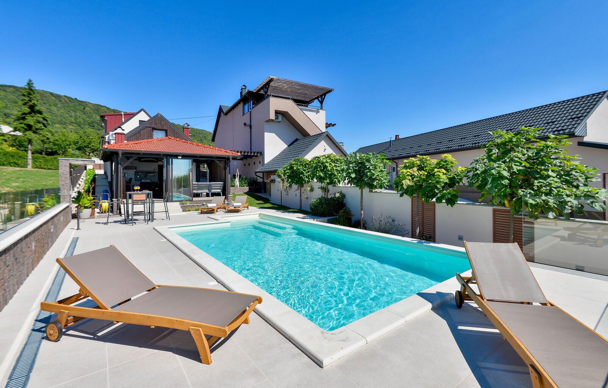 Une piscine avec des chaises longues, un patio couvert et une vue sur les maisons.