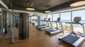 Een fitnessruimte met loopbanden, een roeimachine en een spiegelwand.