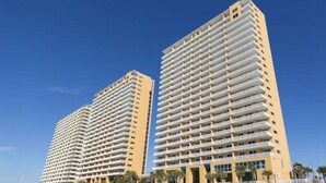 Twee hoogbouwgebouwen met meerdere balkons, waarschijnlijk onderdeel van een hotel of wooncomplex, gelegen nabij een strand.