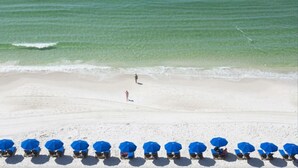 Een strand met helder turquoise water, een zandstrand en rijen blauwe parasols.