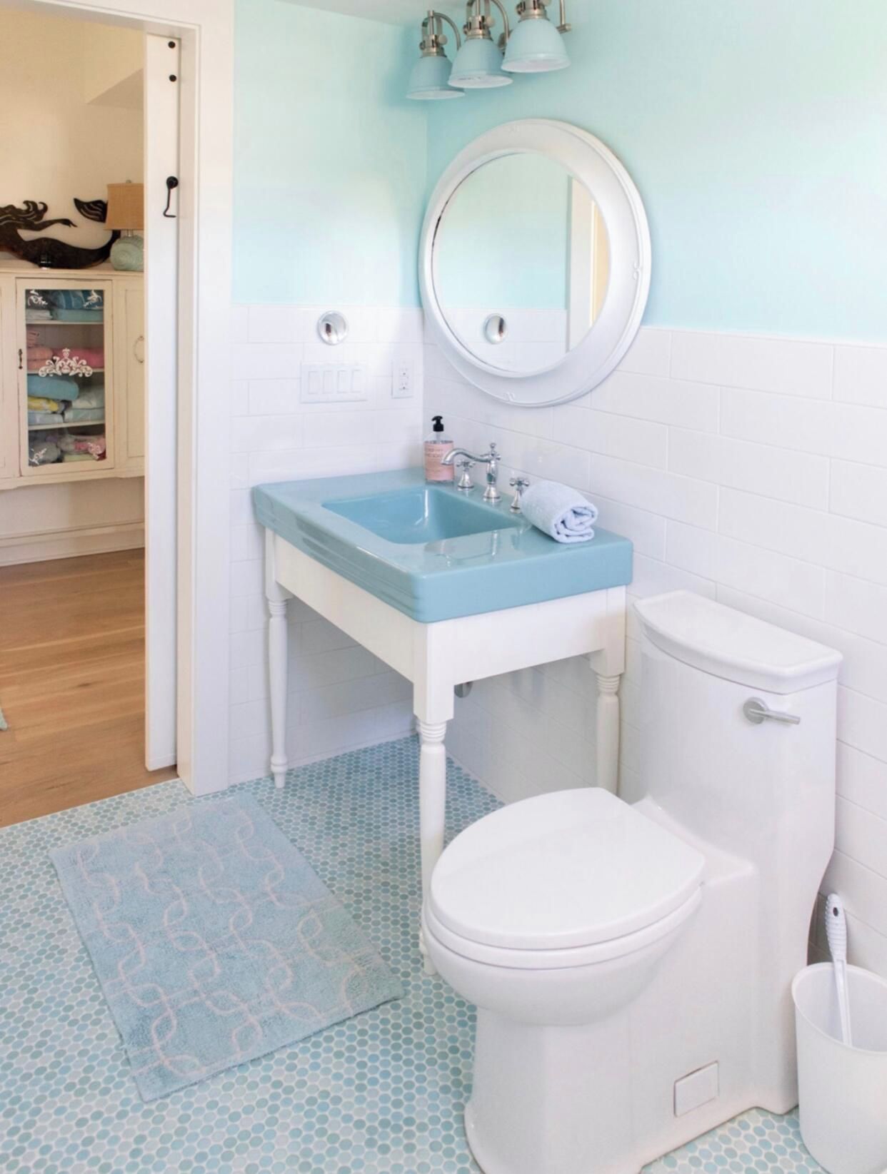 Une salle de bain avec des toilettes blanches, un lavabo bleu et un miroir au-dessus.