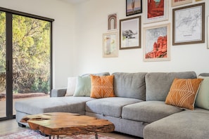 A modern living room with a grey sectional sofa, a wooden coffee table, and a large window offering a view of trees. - Peaceful Sedona Sanctuary I Private Creek Access (Sedona)