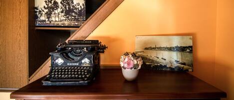 A vintage typewriter on a wooden desk with a vase of flowers and two framed photographs.