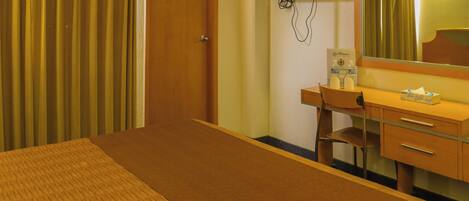 A hotel room with a bed, a desk, a chair, a mirror, a television, and a bottle of water on the desk.