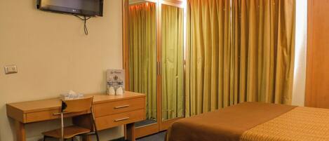 A hotel room with a bed, a desk with a chair, a mirror, and a television on the wall.