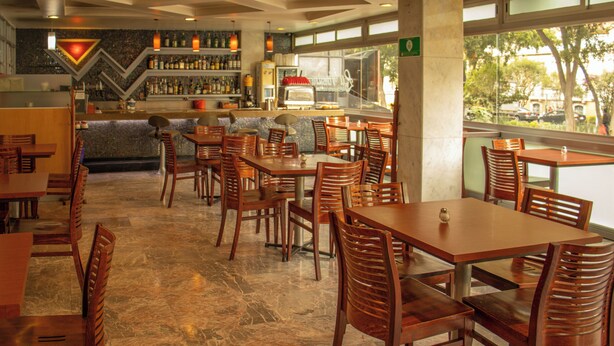 A restaurant with wooden tables and chairs, a bar area, and a view of the outdoors. - Hotel Milan CDMX (Mexico City)