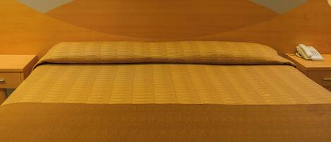 Una habitación de hotel con una cama grande, una mesita de noche con teléfono y un interruptor de luz en la pared.