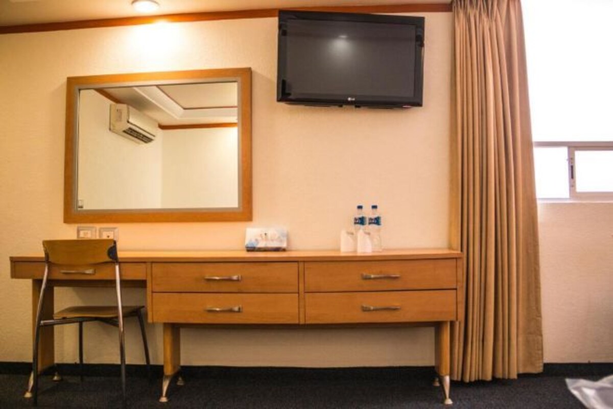 Habitación de hotel con escritorio de madera, una silla, televisor de pantalla plana en la pared y ventana con cortinas.
