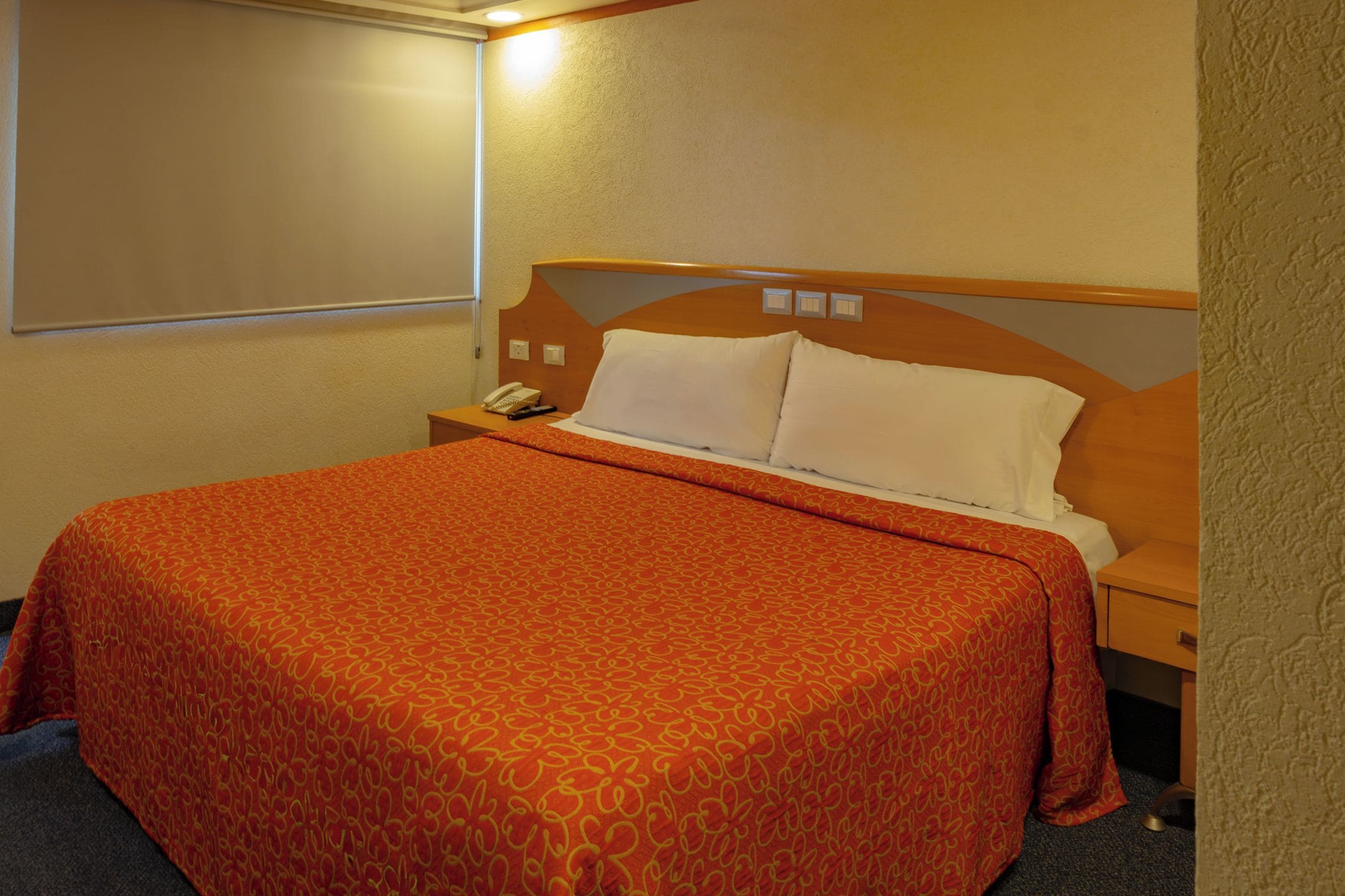 A hotel room with a large bed, a nightstand, a telephone, and a wall-mounted light.