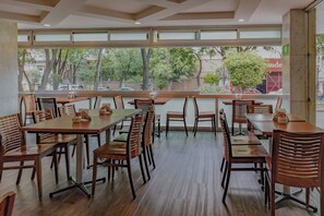 Un amplio comedor interior con varias mesas y sillas de madera, y grandes ventanales que ofrecen vistas al exterior.