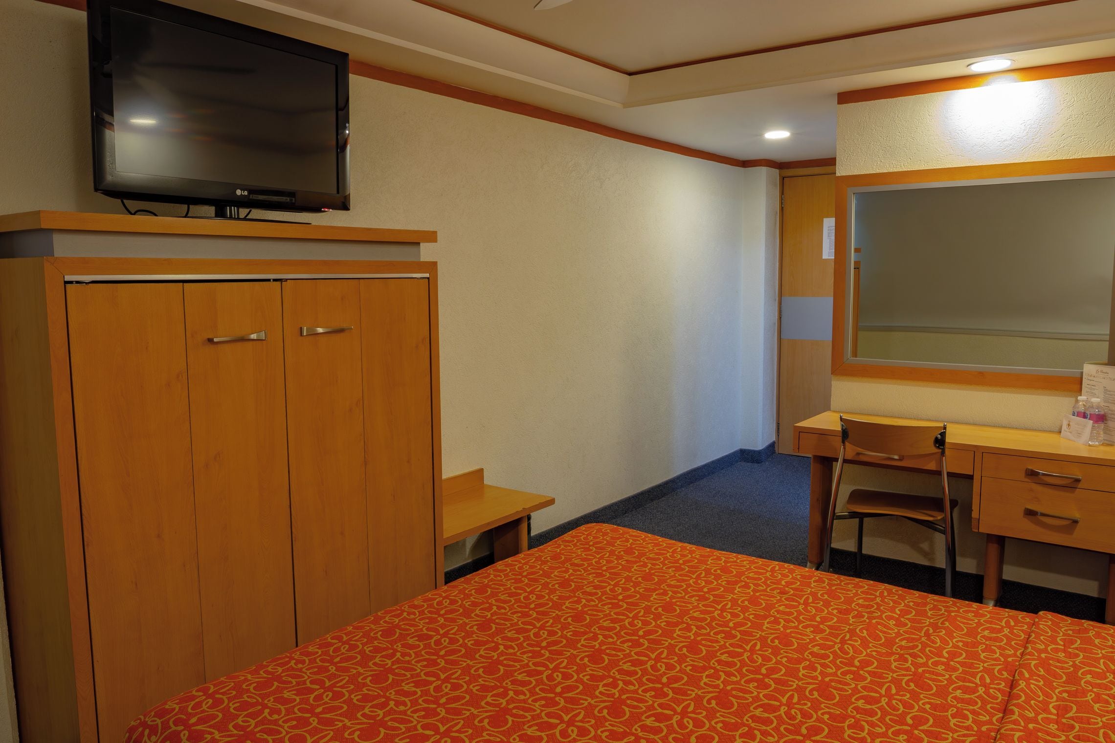 A hotel room with a bed, a desk, a chair, a wardrobe, and a television.