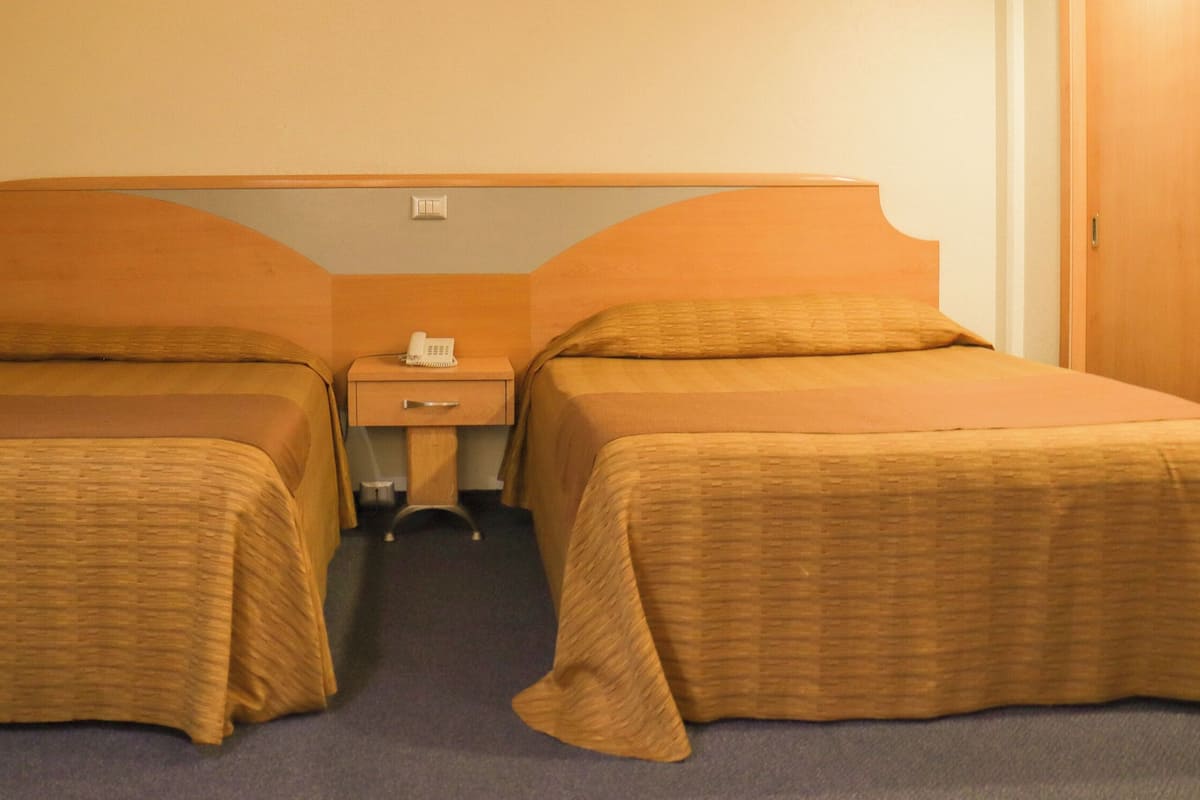 A hotel room with two single beds, a nightstand with a telephone, and a small table.
