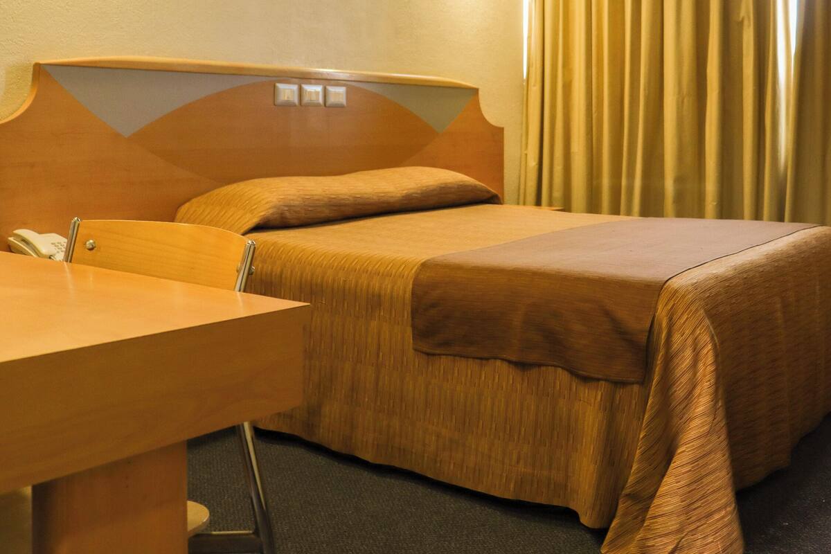 A hotel room with a bed, a desk, and a telephone.