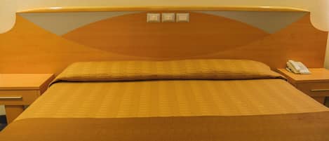 Una habitación de hotel con una cama grande, un cabecero de madera, dos mesitas de noche y un teléfono en una de ellas.