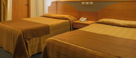 Habitación de hotel con dos camas, cabecero de madera, mesita de noche con teléfono y una puerta.