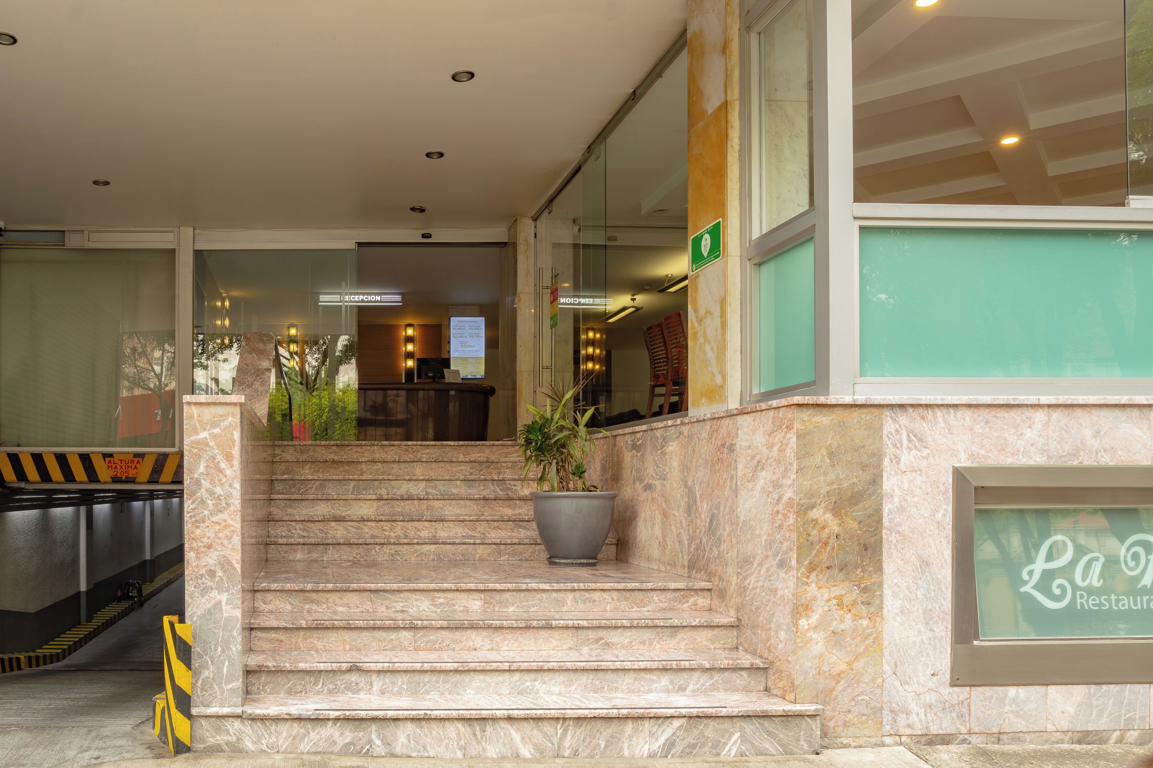 A hotel reception area with a staircase leading to the entrance, a reception desk, and a sign for a restaurant.