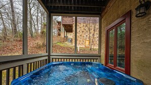 A hot tub on a wooden deck with a stone wall and a window. - Family Cabin Near Dollywood • Theater & Games (Pigeon Forge)
