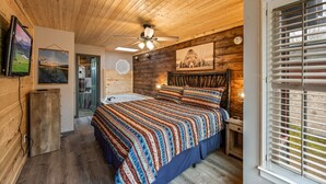 A bedroom with a wooden ceiling, a bed with a patterned bedspread, a ceiling fan, and a window with blinds. - Family Cabin Near Dollywood • Theater & Games (Pigeon Forge)