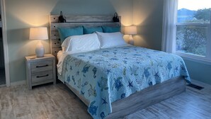 Un dormitorio con cama, mesitas de noche, ventilador de techo y ventana con vistas.