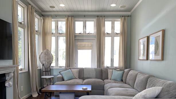 Una sala de estar con sofá modular, chimenea, televisor y ventanas grandes con cortinas.