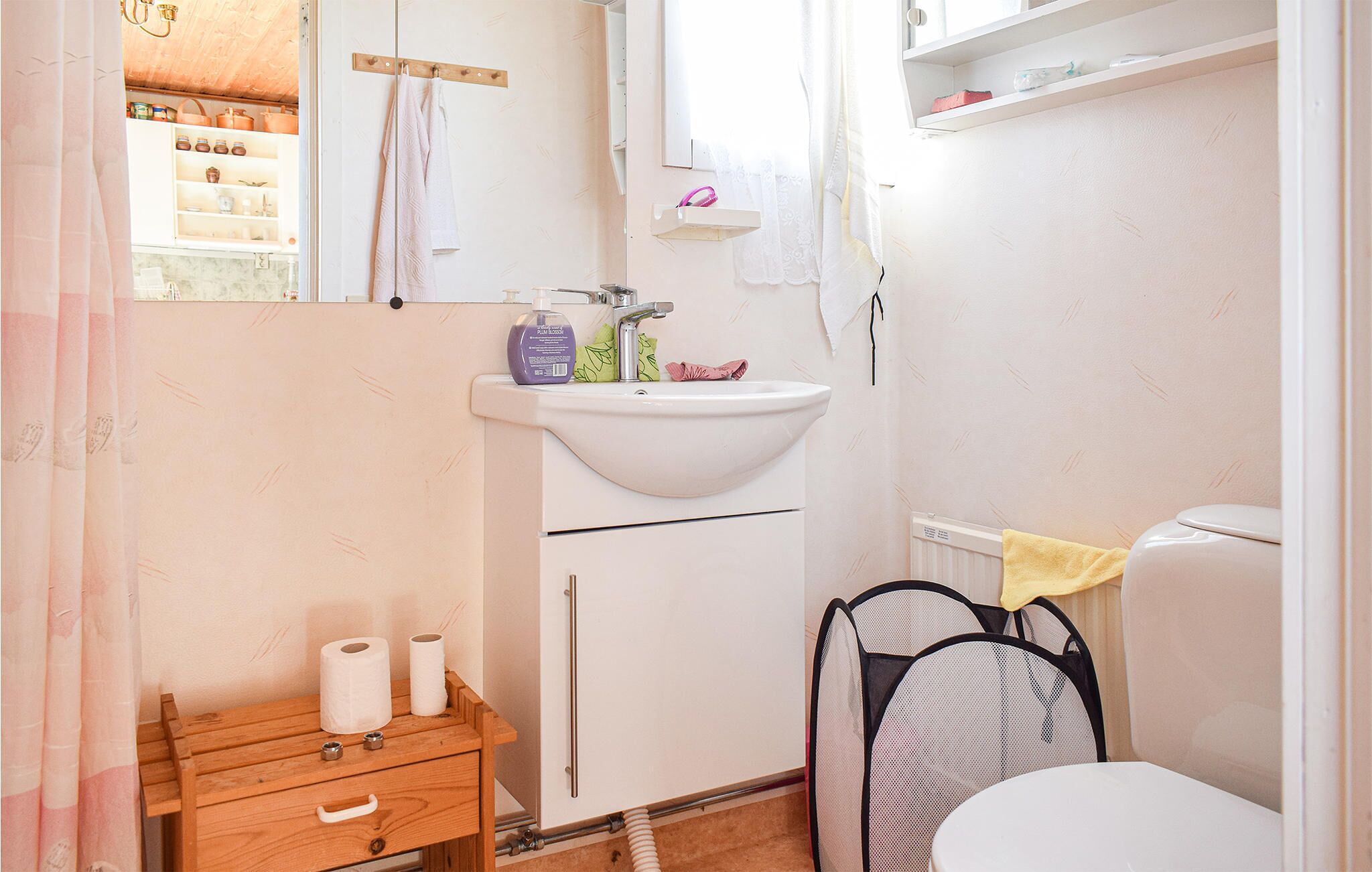 A small, clean bathroom with a sink, toilet, and a wooden cabinet with toiletries.