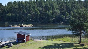 Una piccola baita rossa con un molo su un lago calmo, circondata da una fitta foresta.