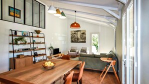 Un vaste espace de vie comprenant une table à manger en bois, des chaises, un canapé et un téléviseur. On y trouve également des étagères avec des plantes et un tableau accroché au mur.