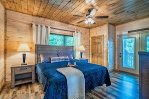 A wooden cabin bedroom with a bed, two nightstands, a ceiling fan, and a door with a view. - Views Putt putt Theater Hot Tub Arcade Pool (Pigeon Forge)